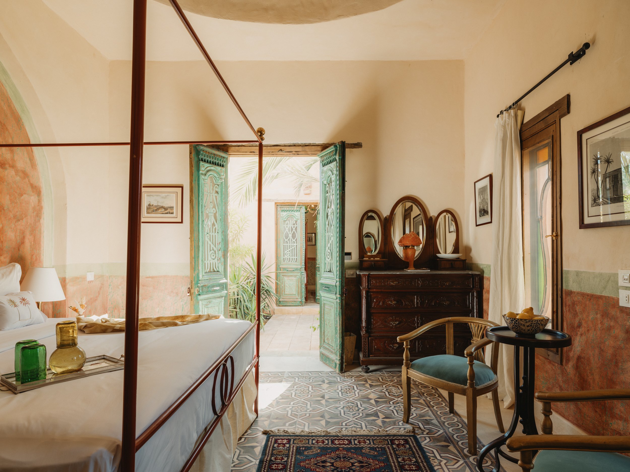 A guest room with a canopy bed, green shutters and antique furniture