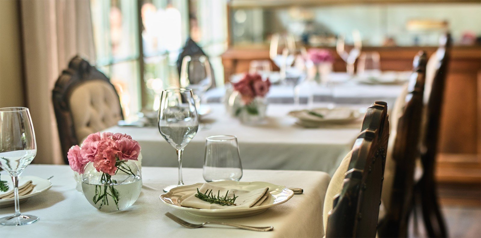 A table laid for dinner with pink flowers and Aegean light through the window