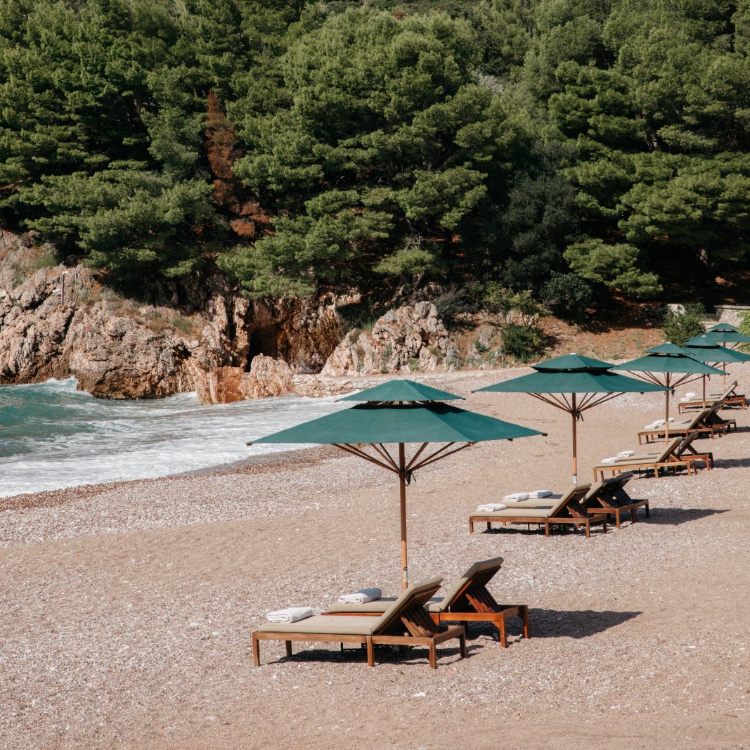 Loungers and green parasols on the pebble sand of Queen's Beach