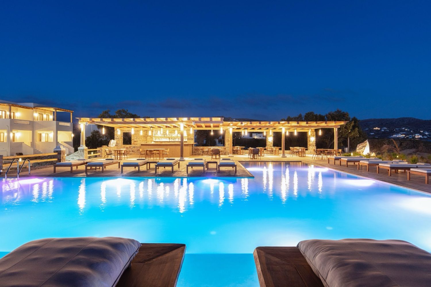 The pool at Ammothines lit at blue hour, the suites and the sea beyond