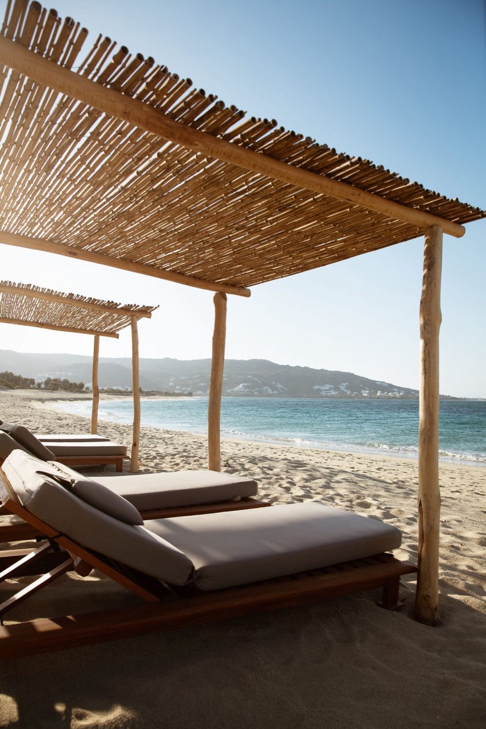 Reed-shaded sunbeds on Plaka beach looking out to the sea and an islet