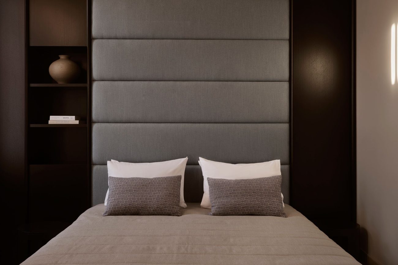 A room in dark timber and grey with a soft upholstered headboard and a reading light