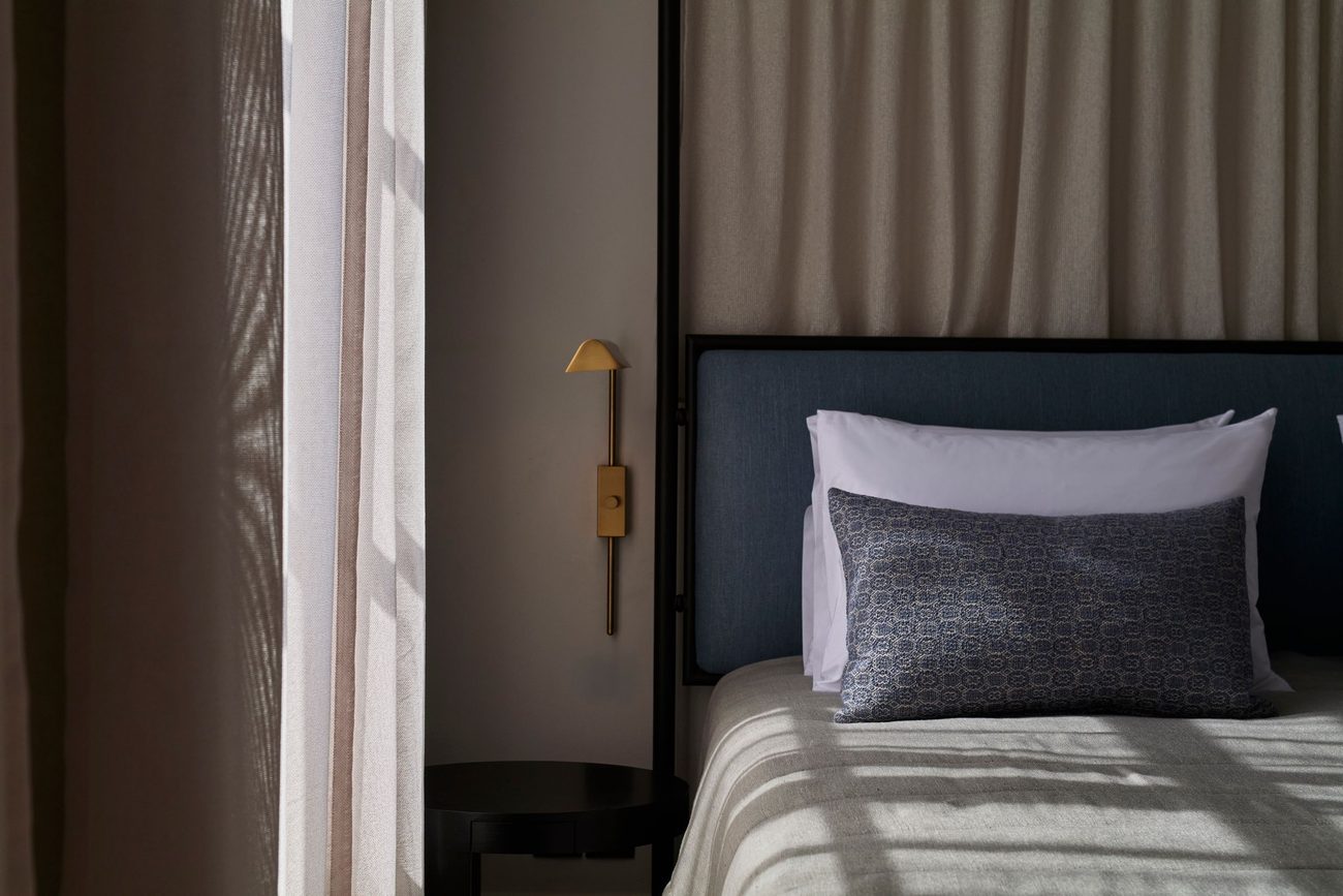 A bedroom in warm neutrals with a blue headboard and a brass wall light