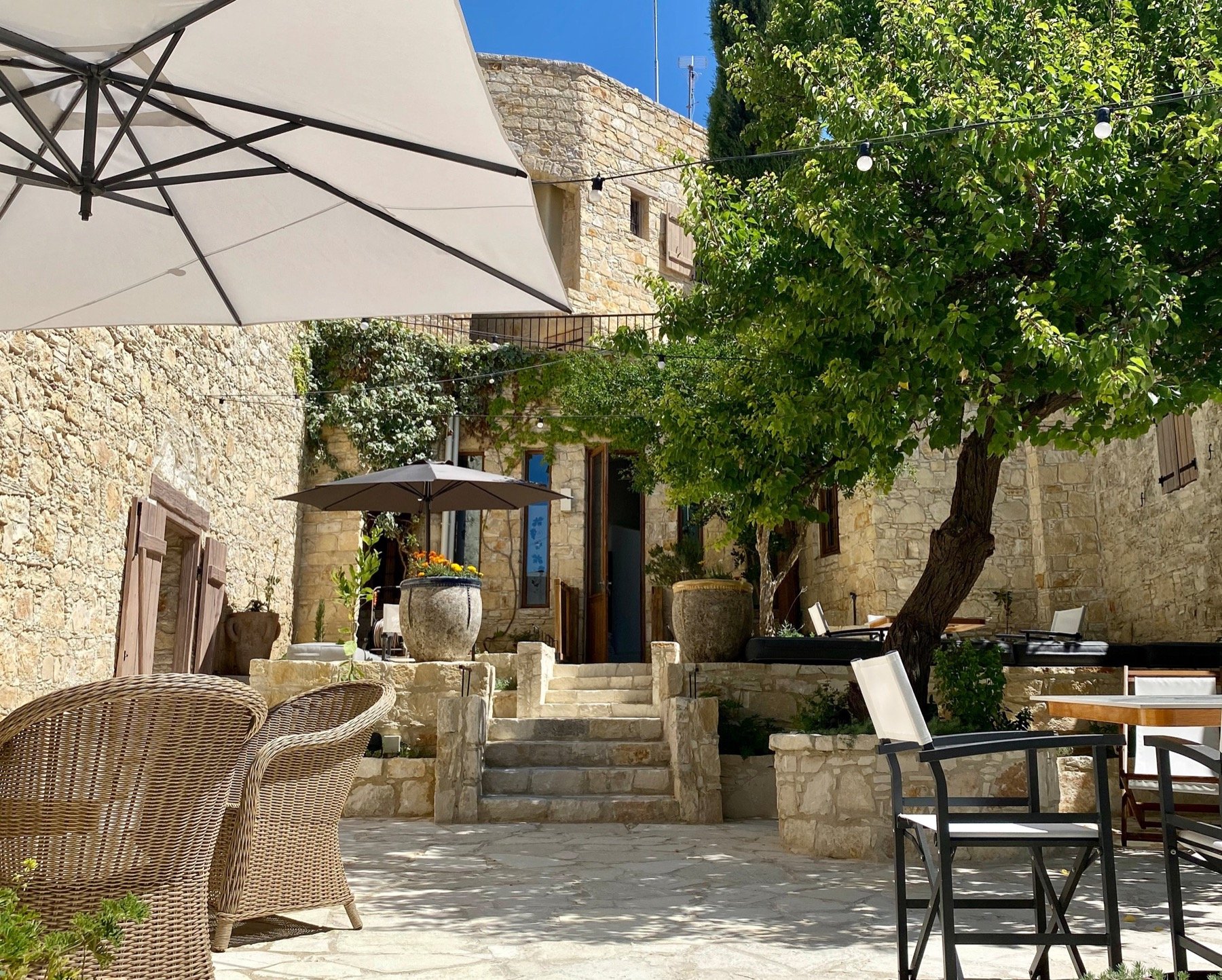A stone courtyard shaded by a tree, with tables set for dinner