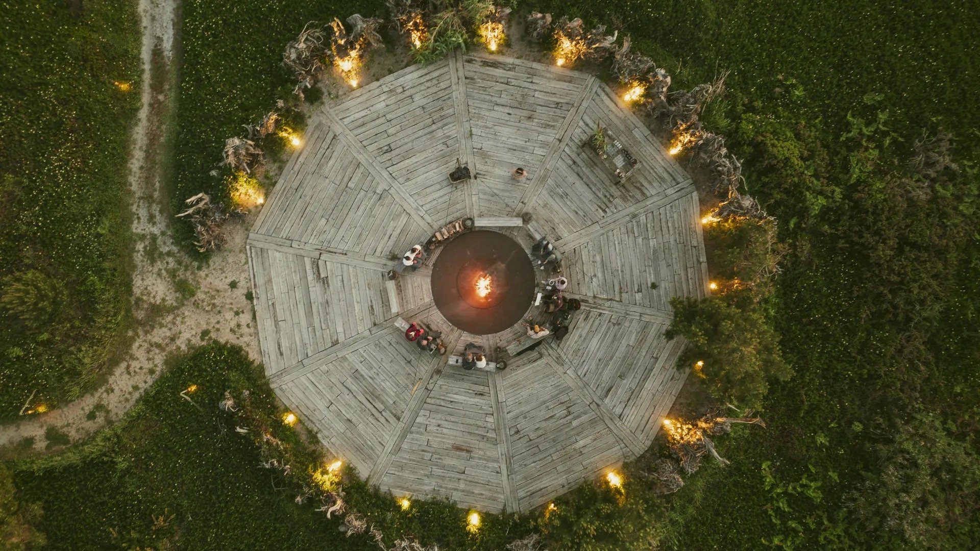 The communal fire circle, a round timber deck around an open fire in the dunes at dusk