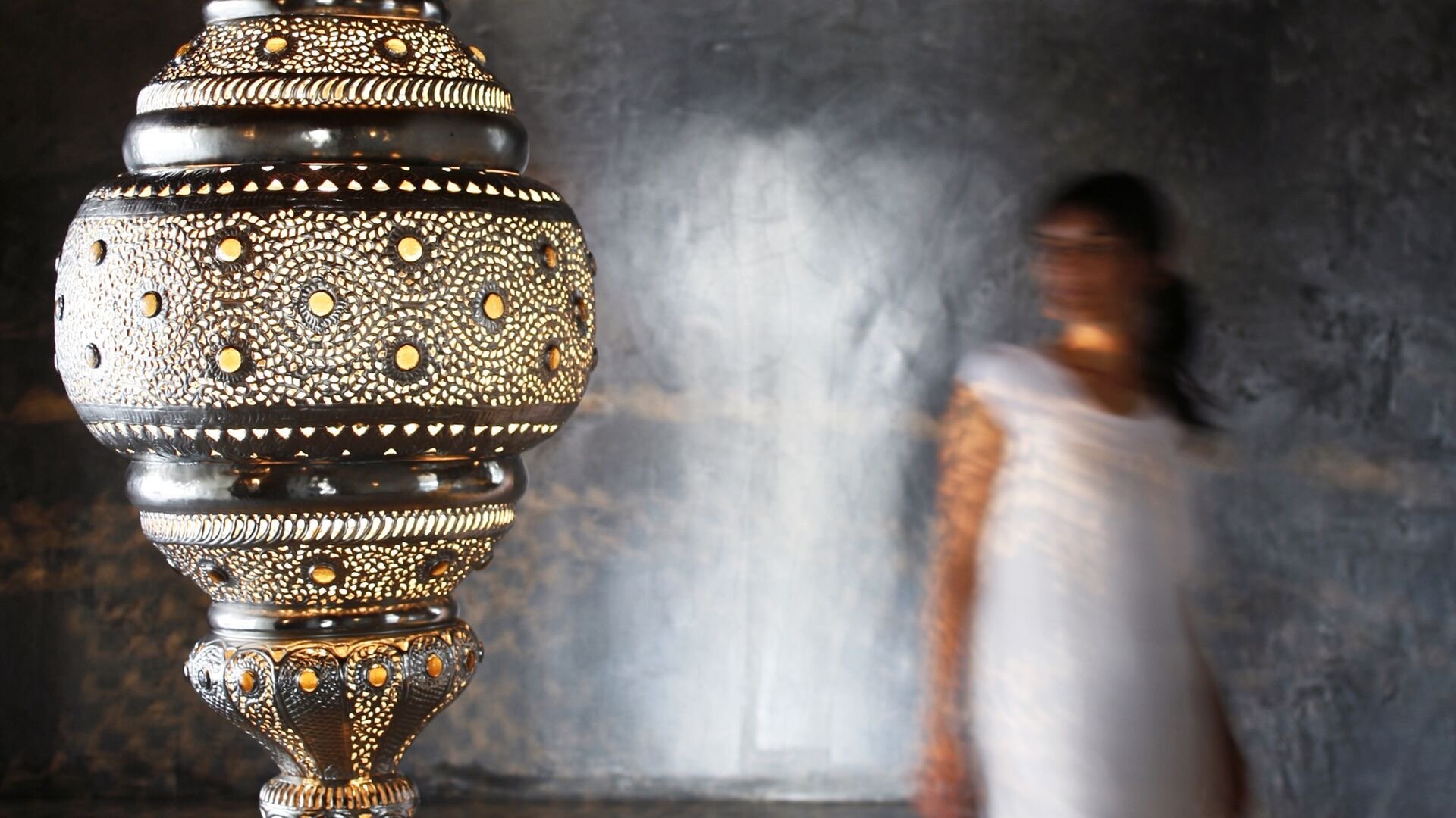 A pierced metal lantern glowing in the spa, a figure passing the polished-plaster wall