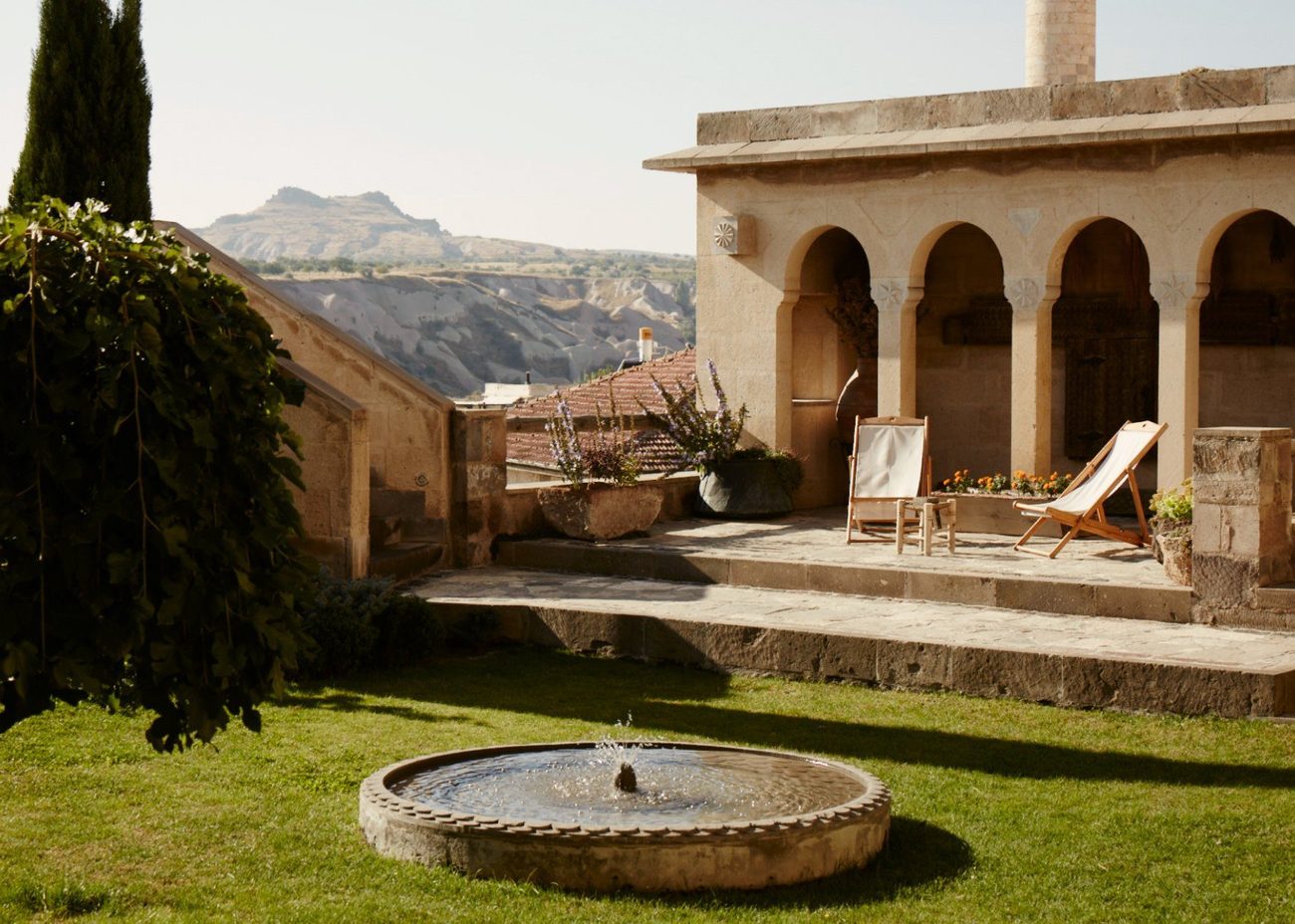 A stone courtyard with arches and a fountain looking out over the valley