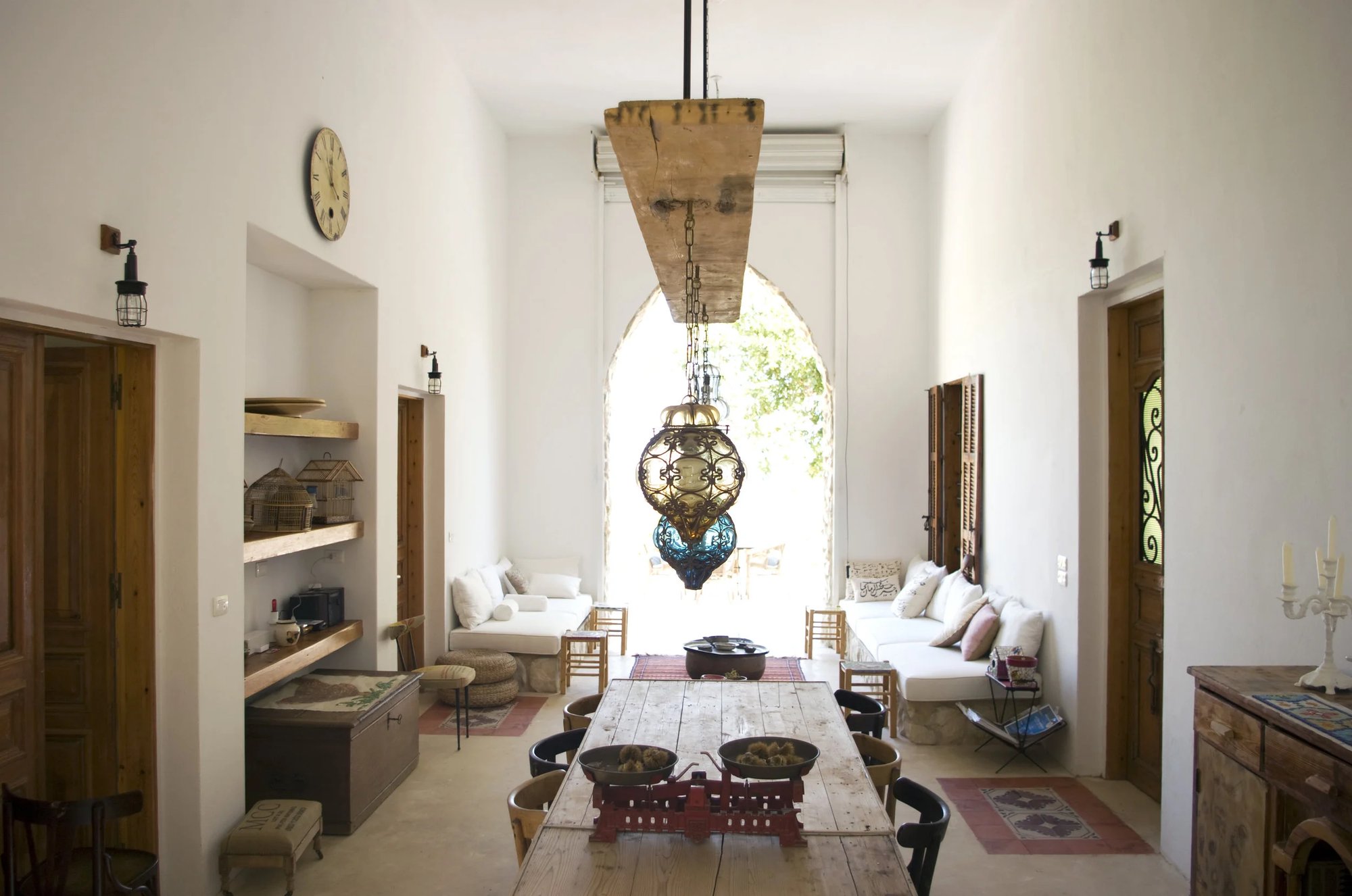 The tall central liwan with a long table under a blue lantern and an arched doorway to the garden