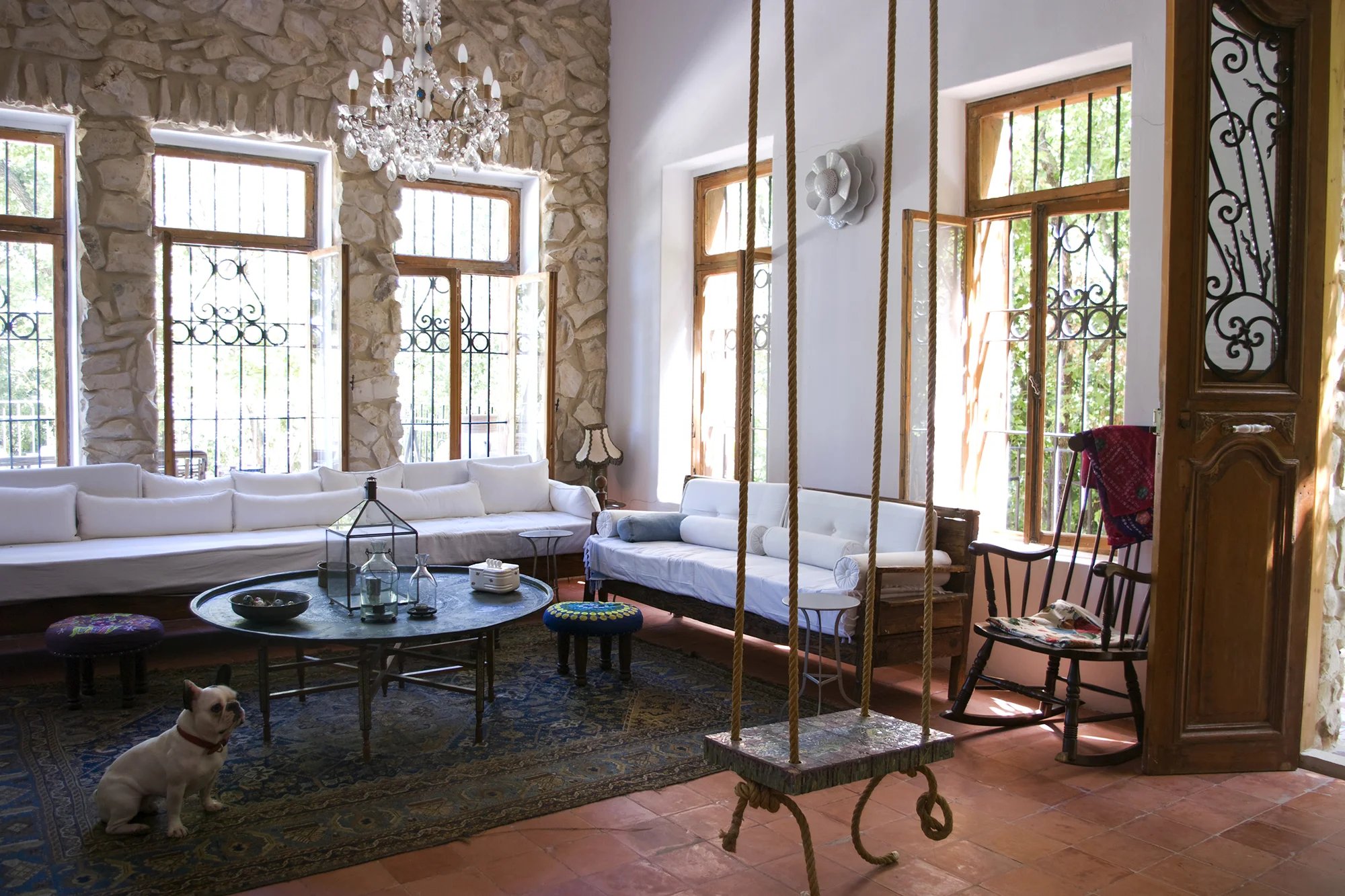 A stone-walled sitting room with white sofas, a rope swing and a French bulldog on the rug