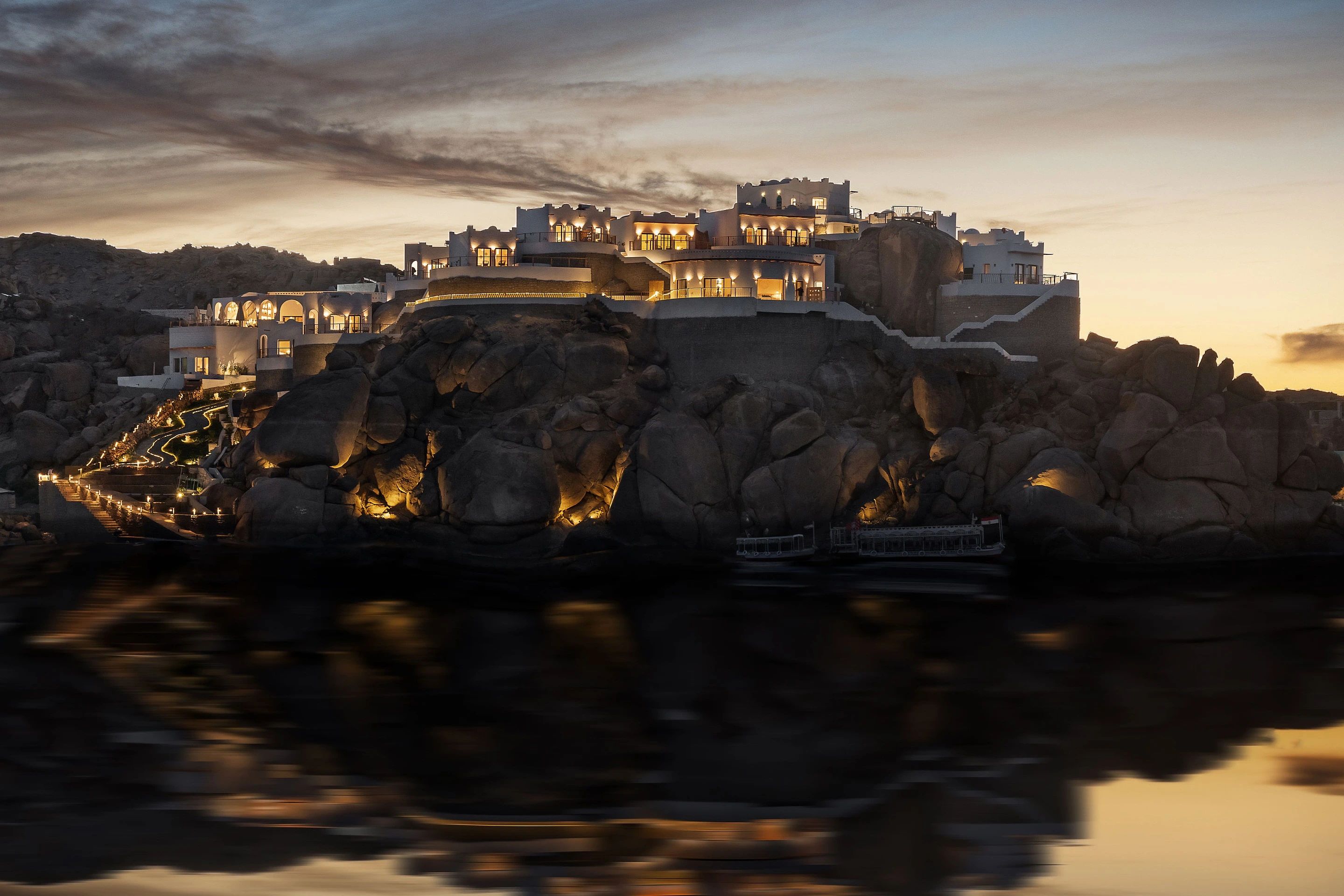 BenBen by Dhara at dusk, its white terraced rooms lit on the granite of a Nile island, feluccas moored at the water below