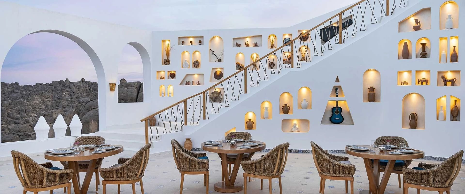 The dining room at BenBen by Dhara, white walls set with lit niches of Nubian pottery, a staircase climbing through them and round tables laid below