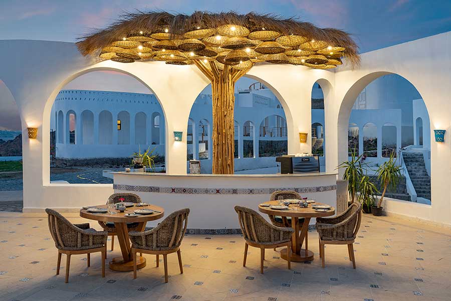 The restaurant under a woven palm canopy, arches open to the river at dusk