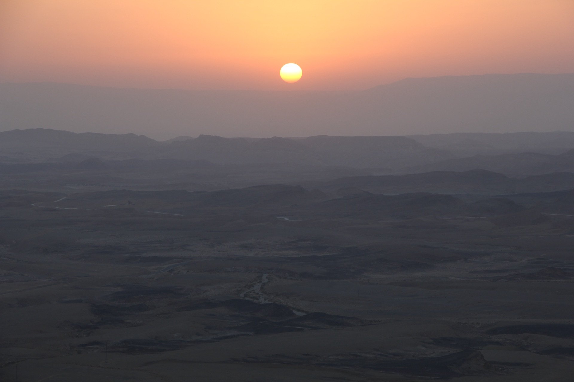 Sunrise over Makhtesh Ramon, the sun low over the hazed ridges of the Negev desert seen from the Mitzpe Ramon rim