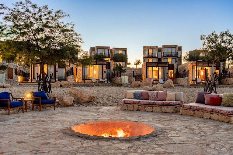 A sunken fire pit and low seating among the stone villas at dusk