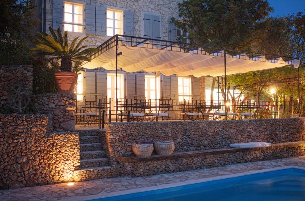 The stone house and its awning-shaded terrace above the pool at dusk