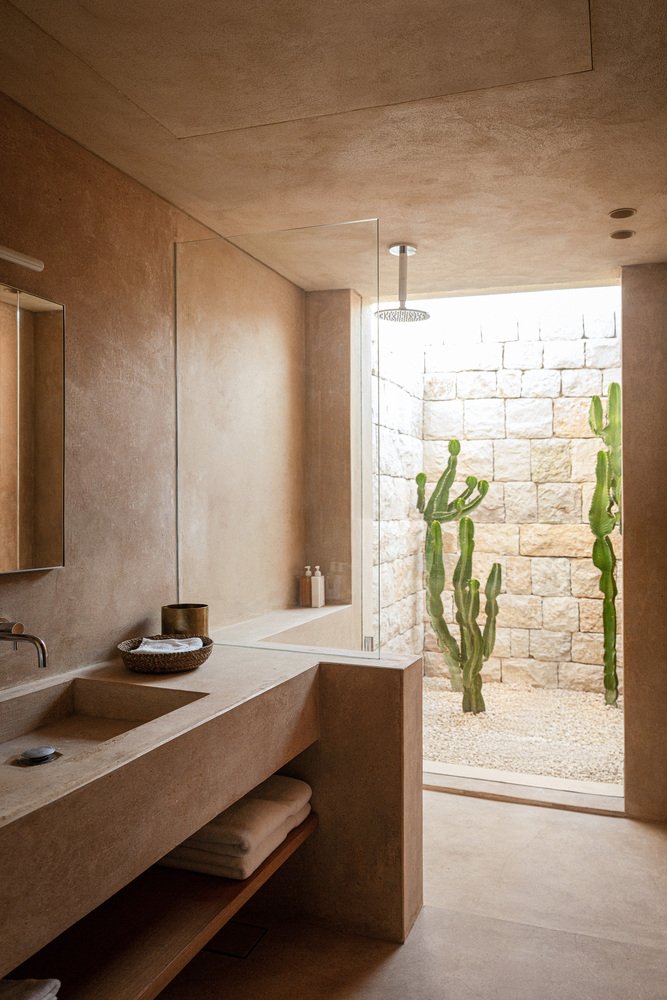 A sand-toned bathroom with a rain shower beside a cactus courtyard
