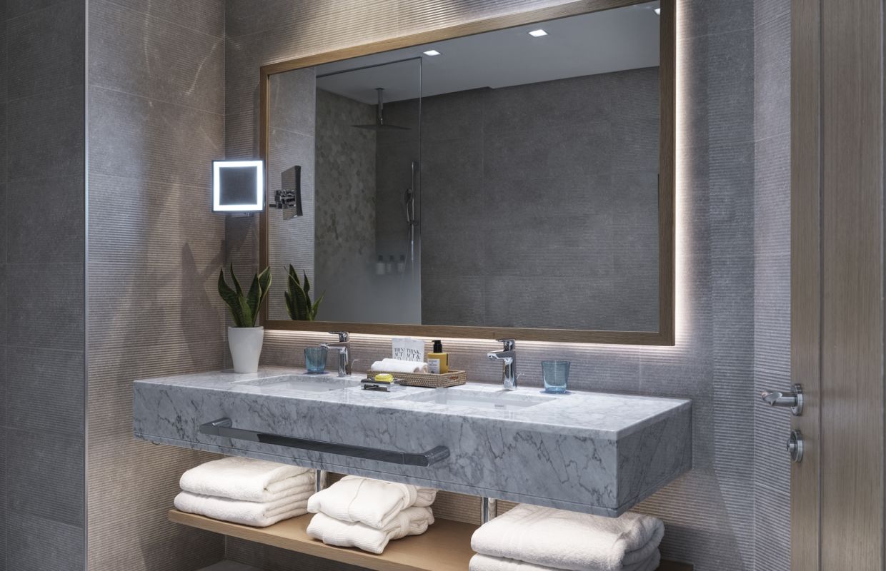 A bathroom with a marble double vanity and backlit mirror