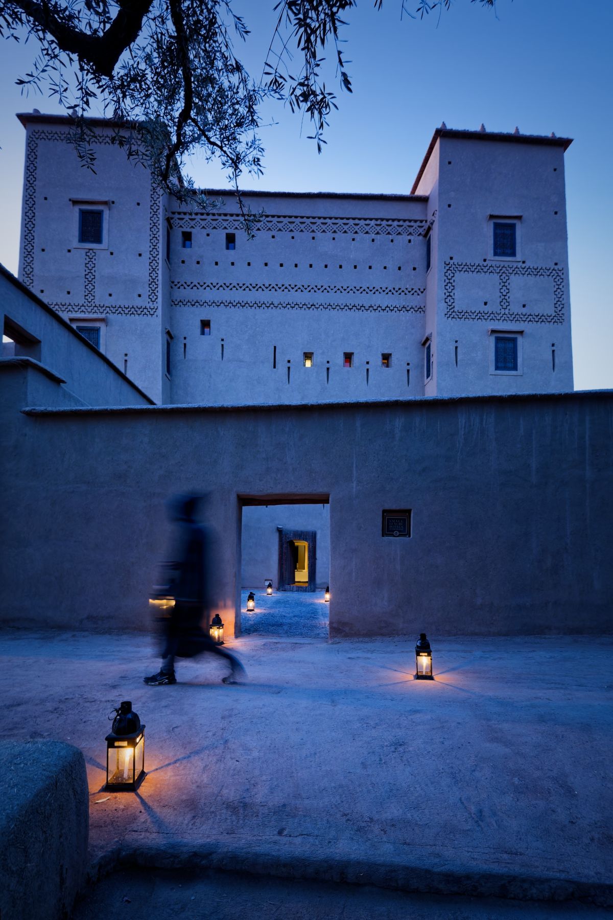 The kasbah's patterned earthen towers at dusk, lanterns lighting the courtyard
