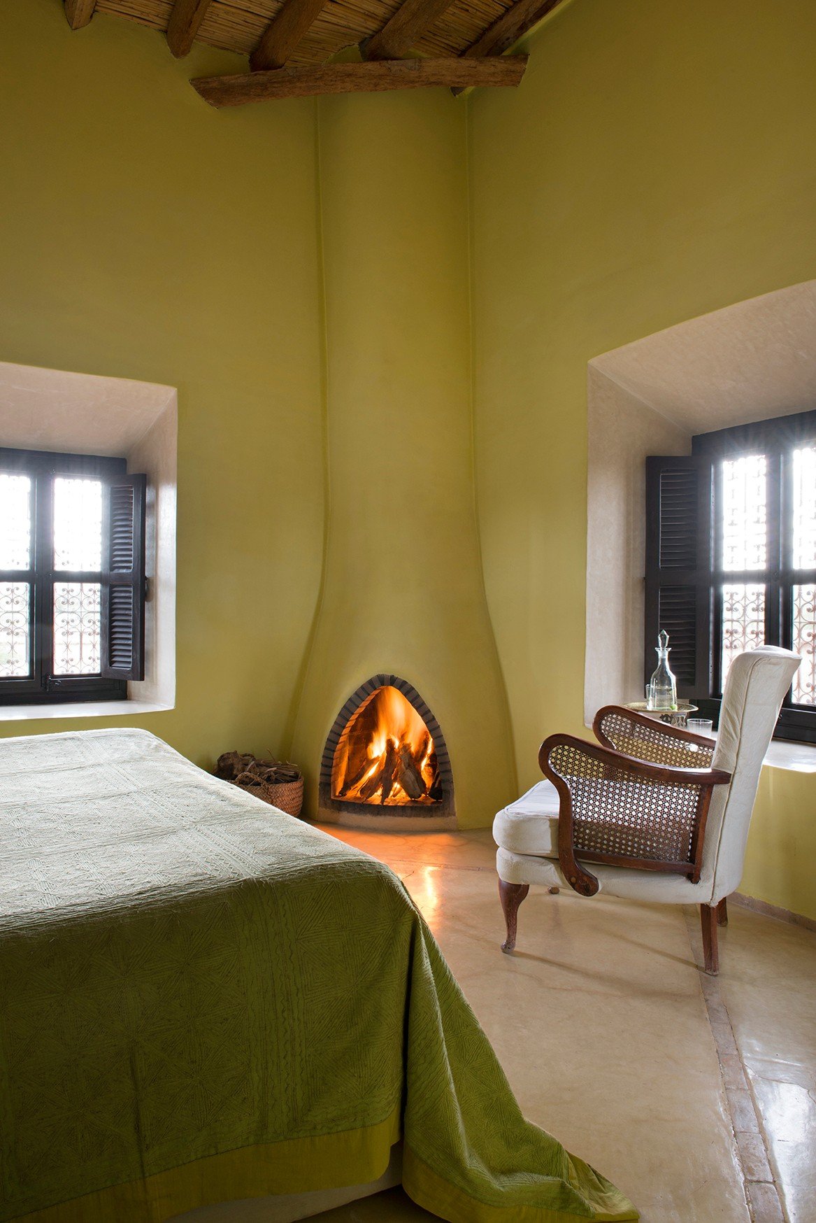 A suite with ochre walls, a lit corner fireplace and shuttered windows