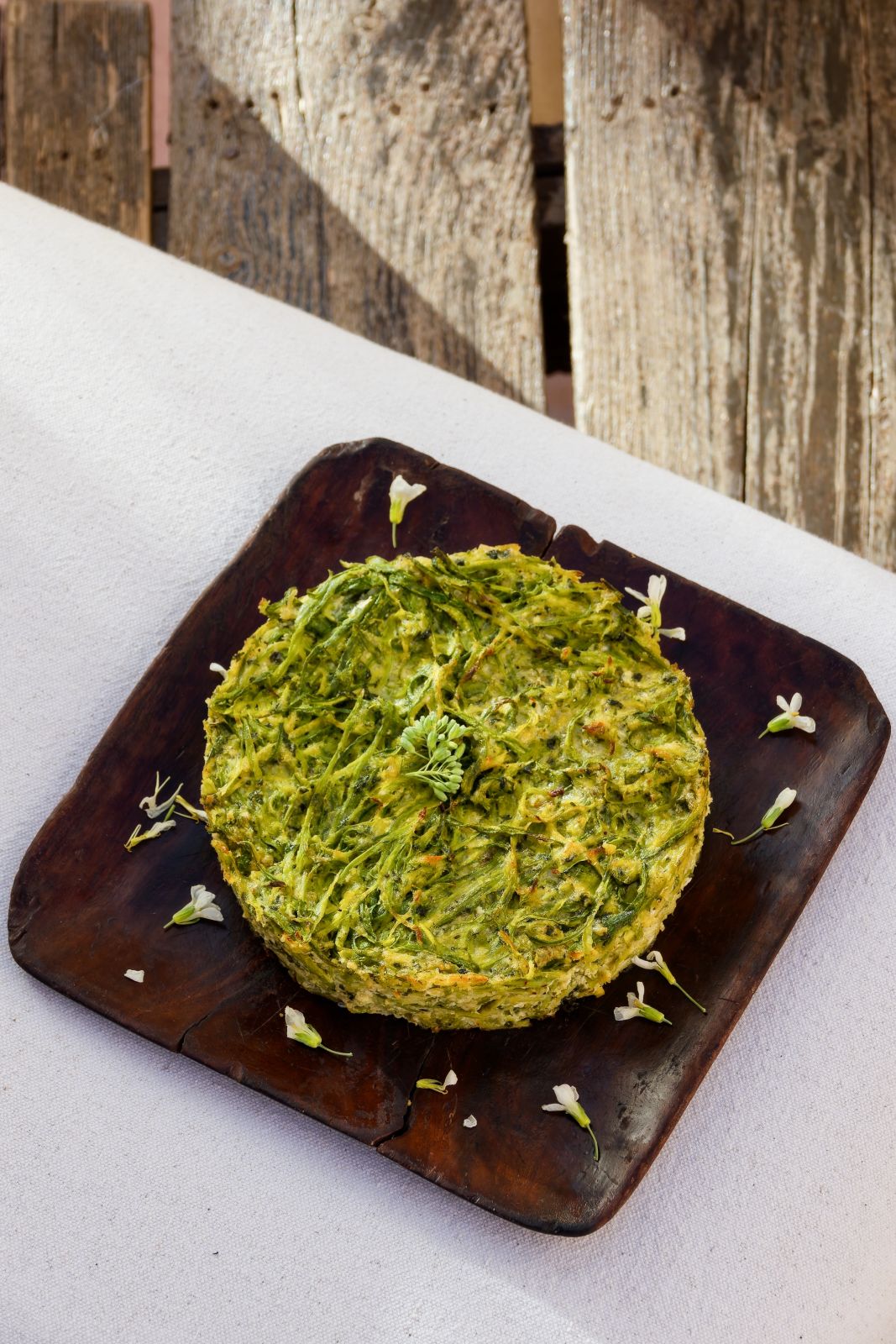 A plant-based dish on a dark wooden plate, scattered with small flowers