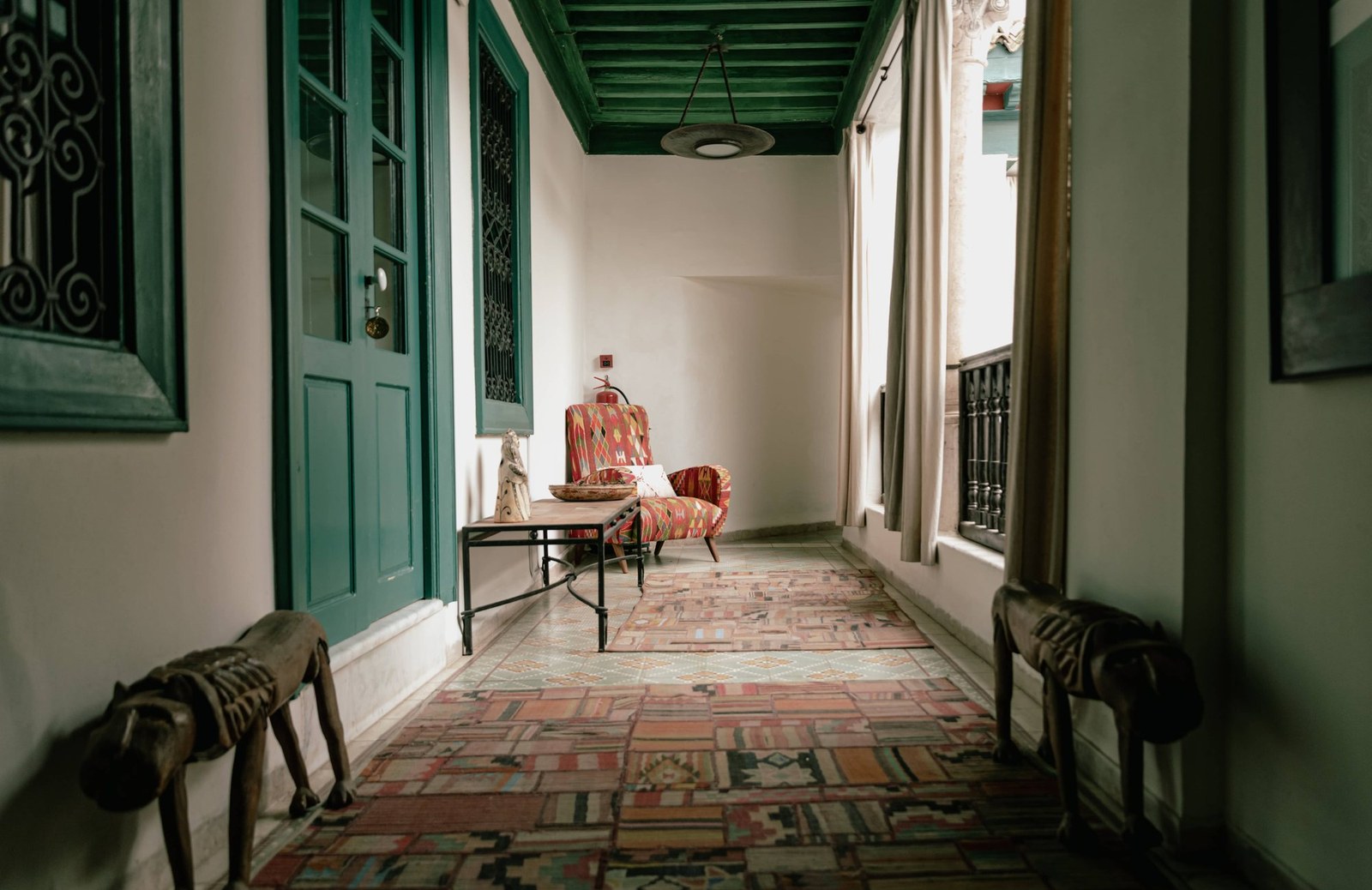 A green-painted gallery of the dar with carpets and a seated figure in traditional dress at the far end
