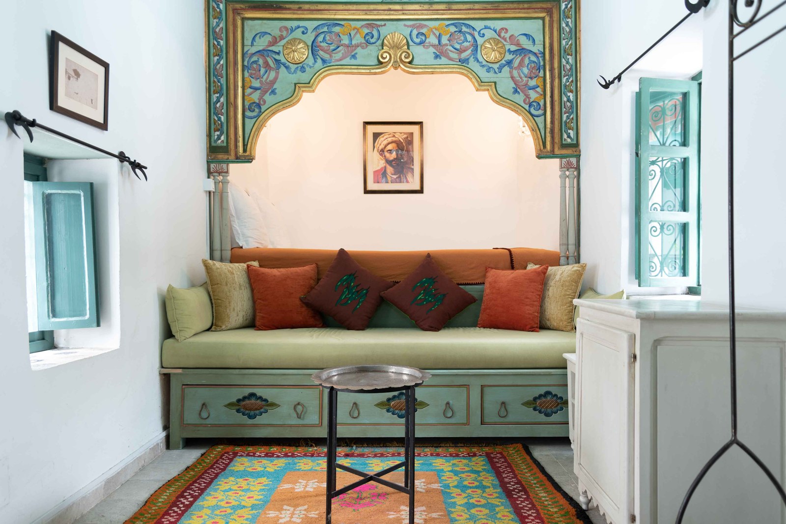 A room with a green tiled banquette, painted arch and patterned cushions
