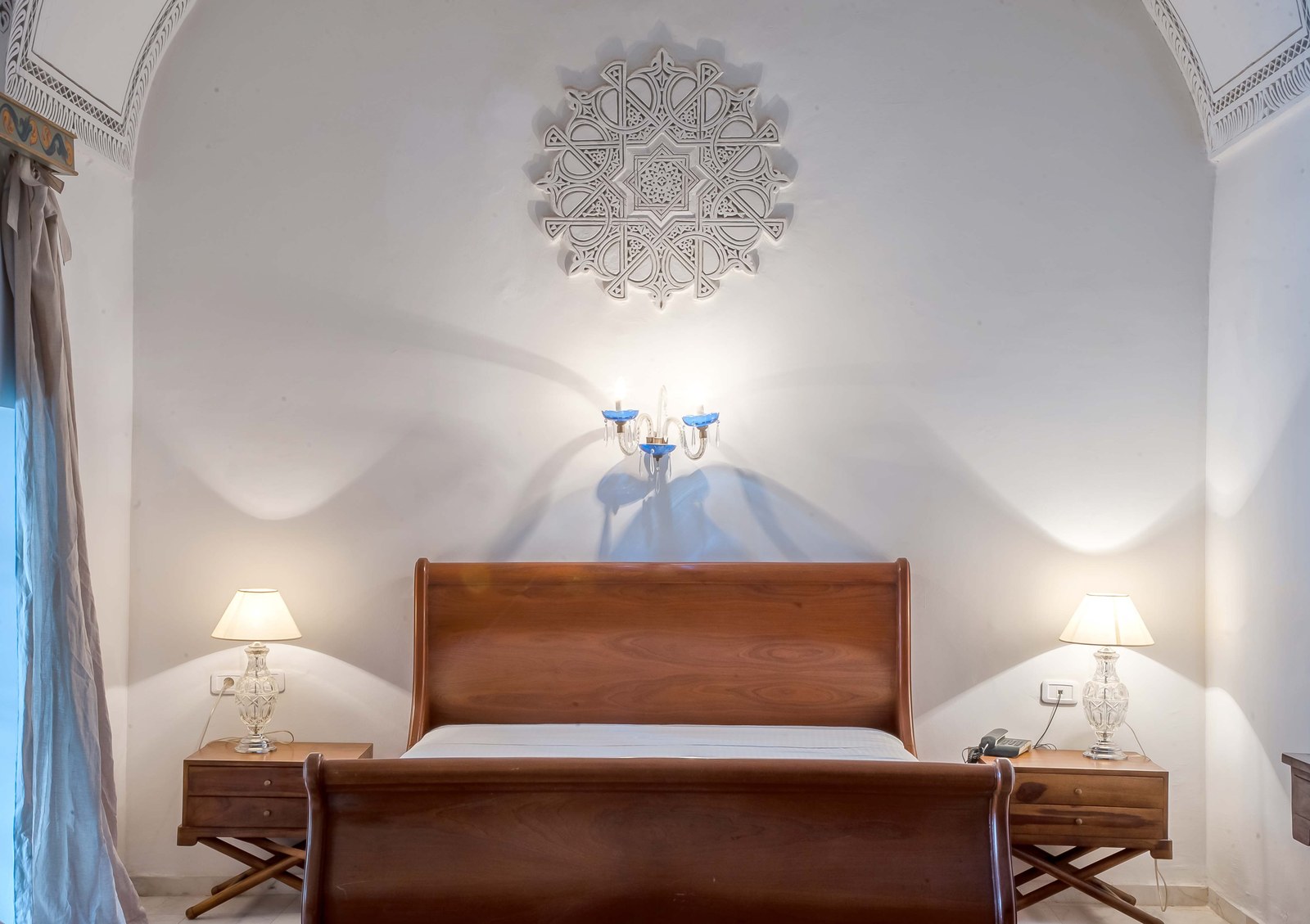 A whitewashed vaulted room with a carved plaster medallion and a wooden bed