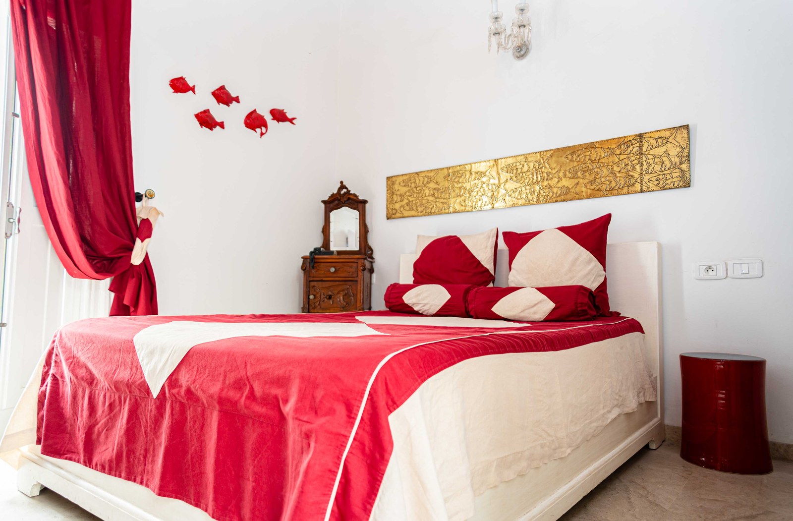 A canopy bed hung in red with matching bedcover in a whitewashed room