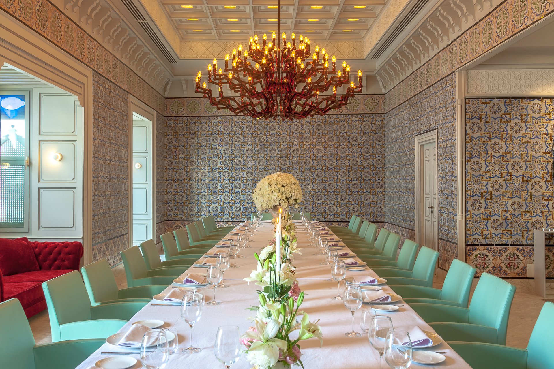 A tiled reception room set for dinner beneath a red chandelier