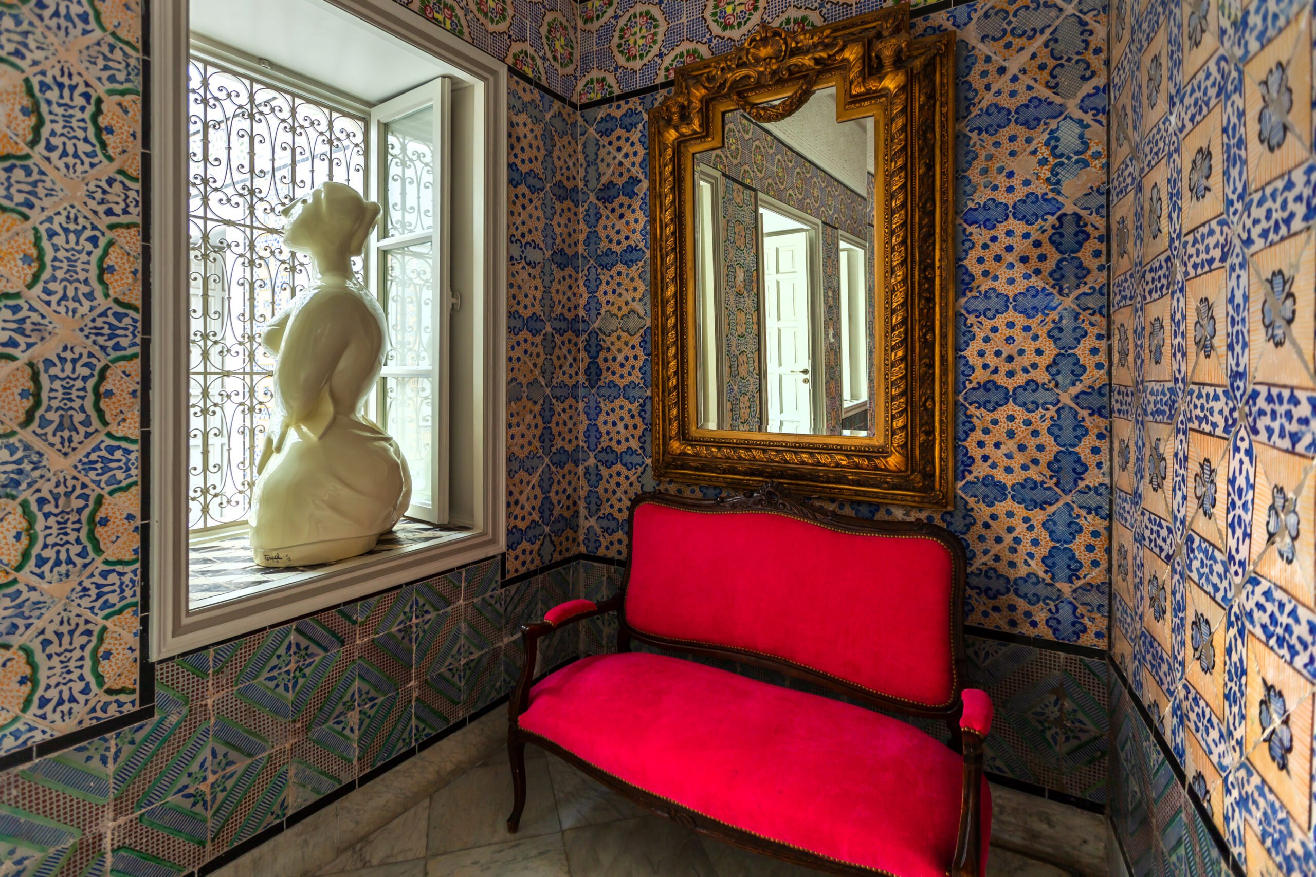 A corner of blue Tunisian tilework with a gilt mirror and a red bench
