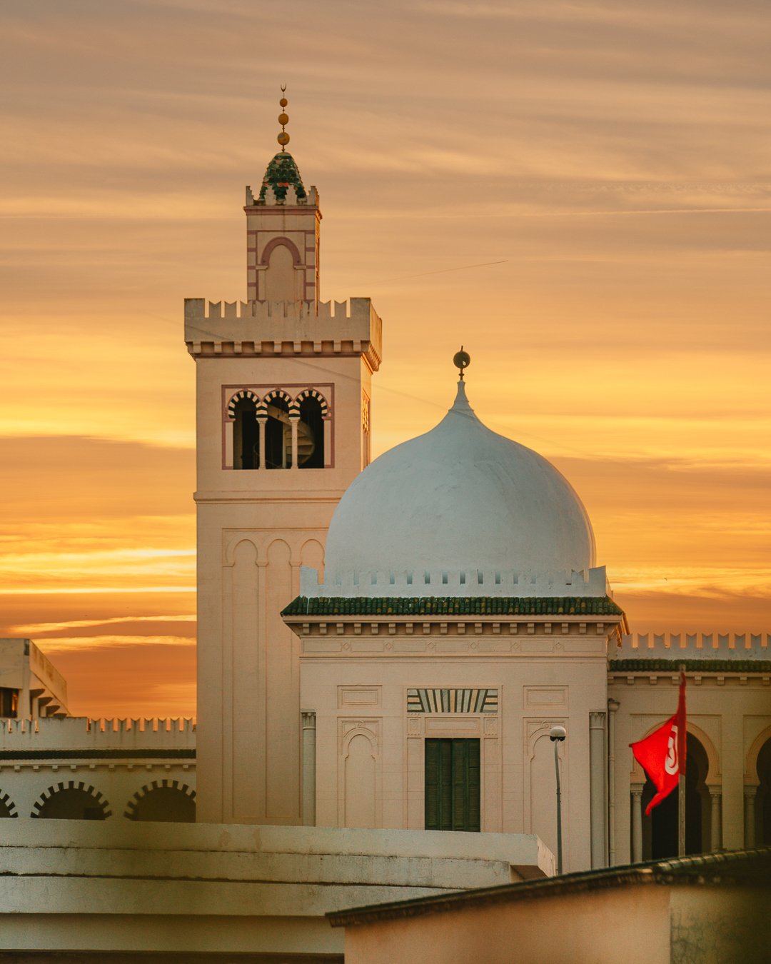 A minaret and white dome of the medina against a sunset sky