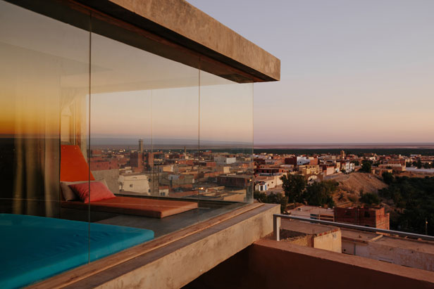 A glass-walled terrace suite looking over the rooftops of Nefta at dusk