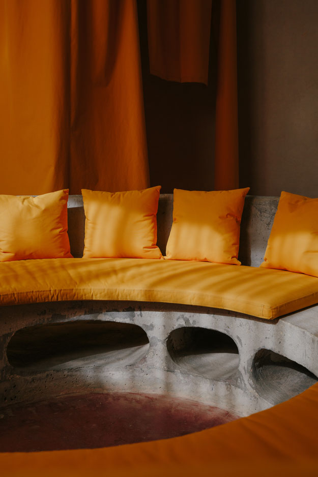 A curved concrete bench with saffron-yellow cushions in a guest room