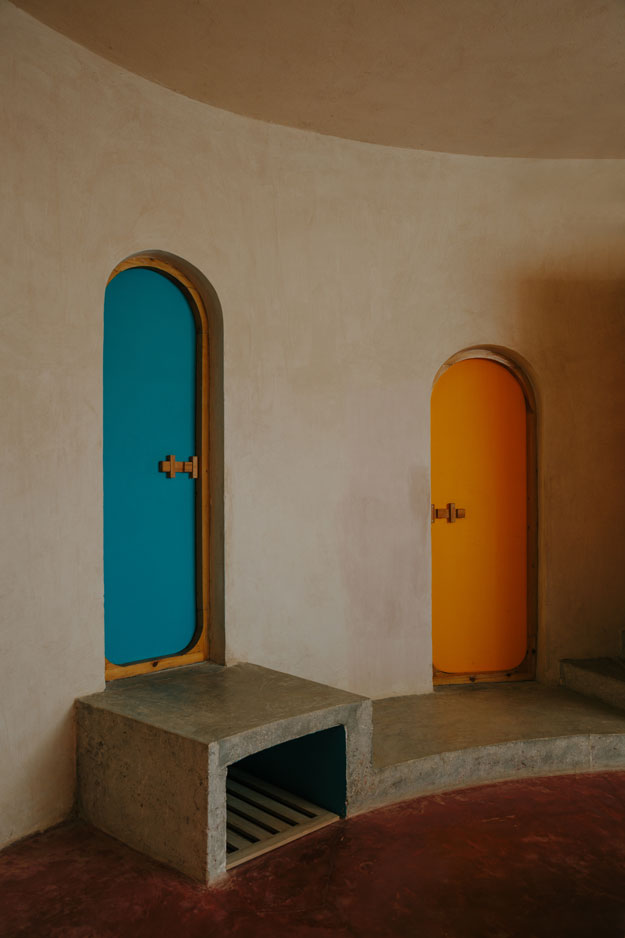 Two arched doors, one blue and one yellow, in a rounded clay-plastered room