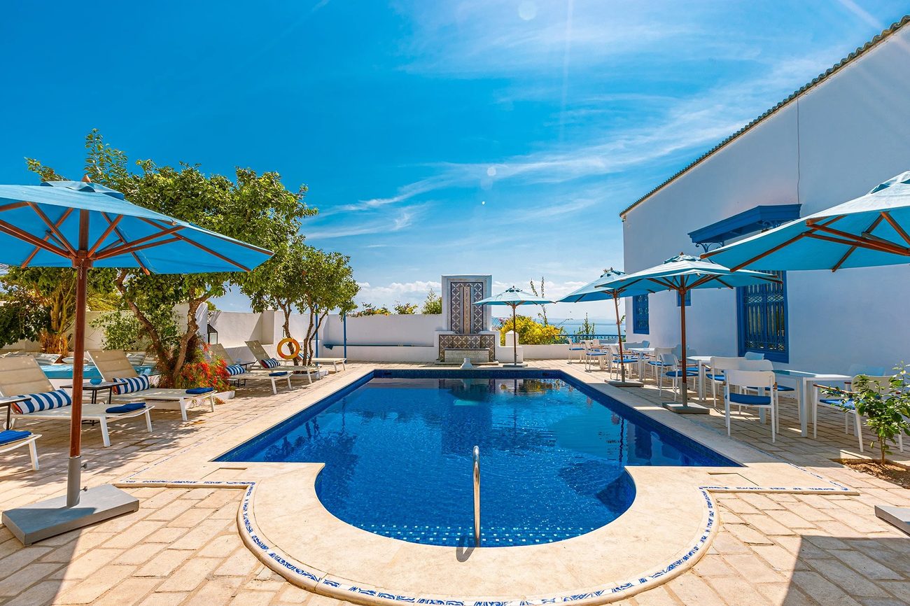 The outdoor pool with striped parasols and the Gulf of Tunis beyond
