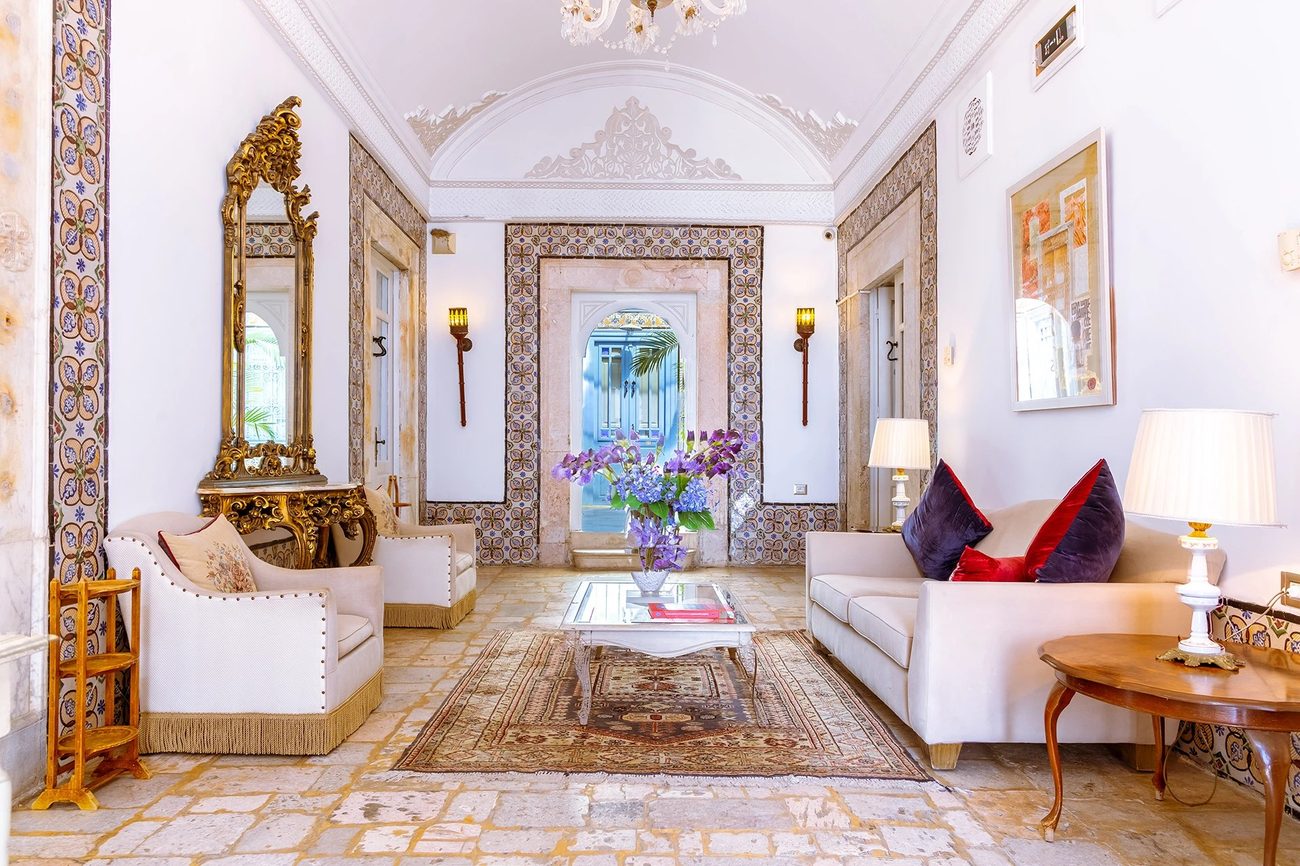 A salon with a tiled floor, a gilt mirror and white sofas