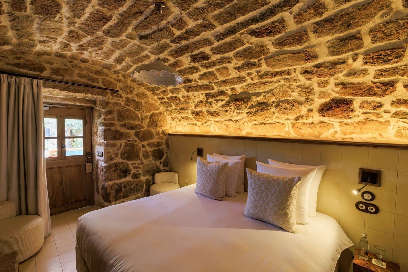 A bedroom beneath a vaulted granite ceiling, with lime-washed walls and a low bed