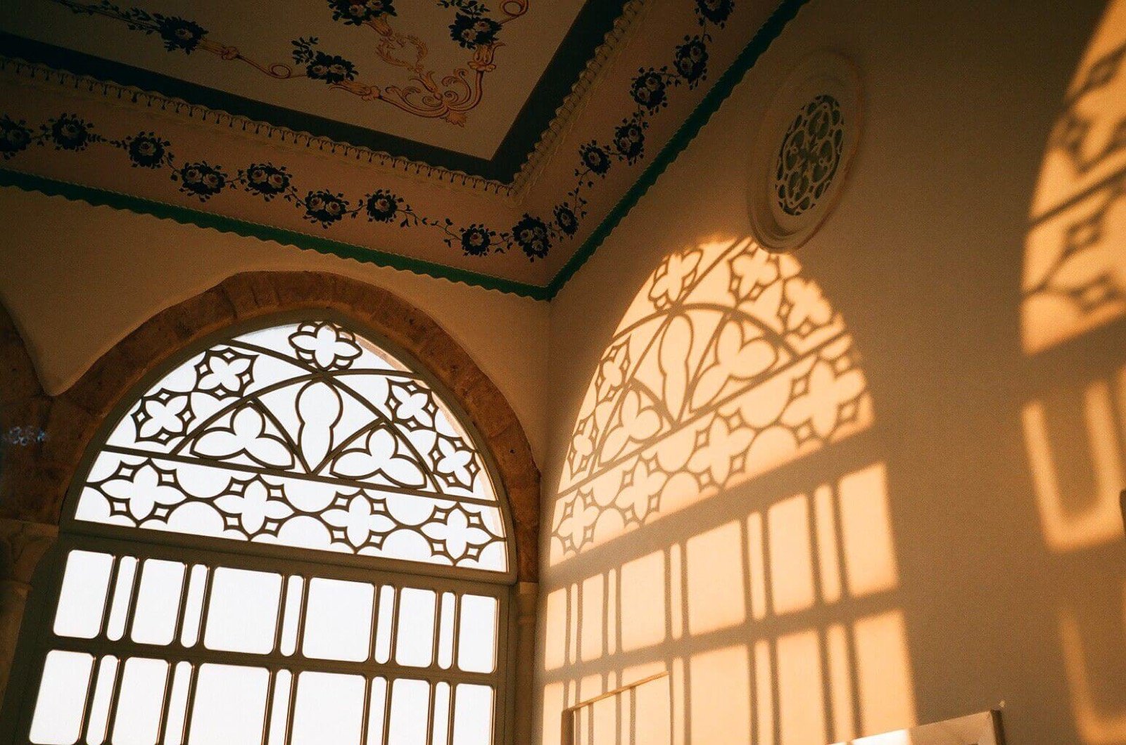 A painted ceiling and a latticed arched window throwing patterns across the wall