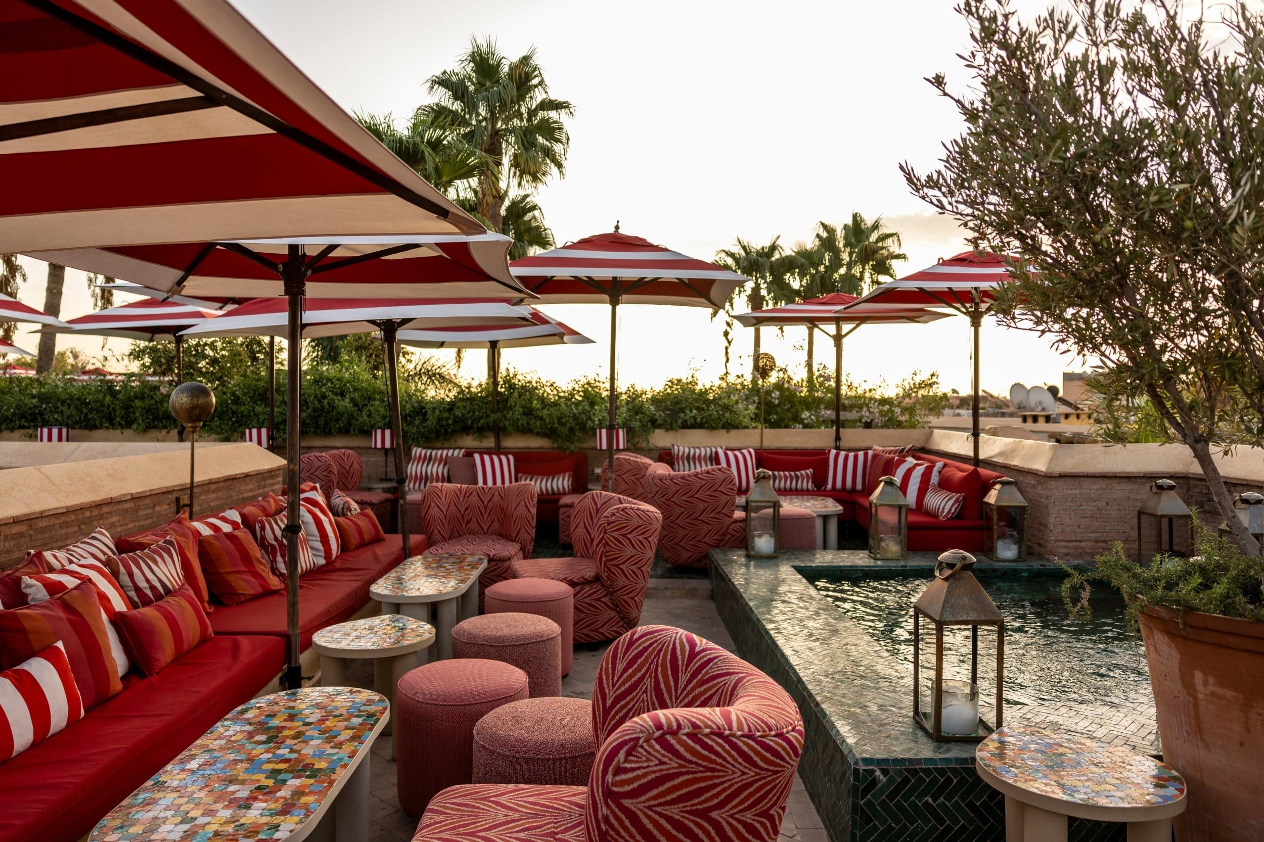 A rooftop plunge pool ringed by red seating and striped parasols
