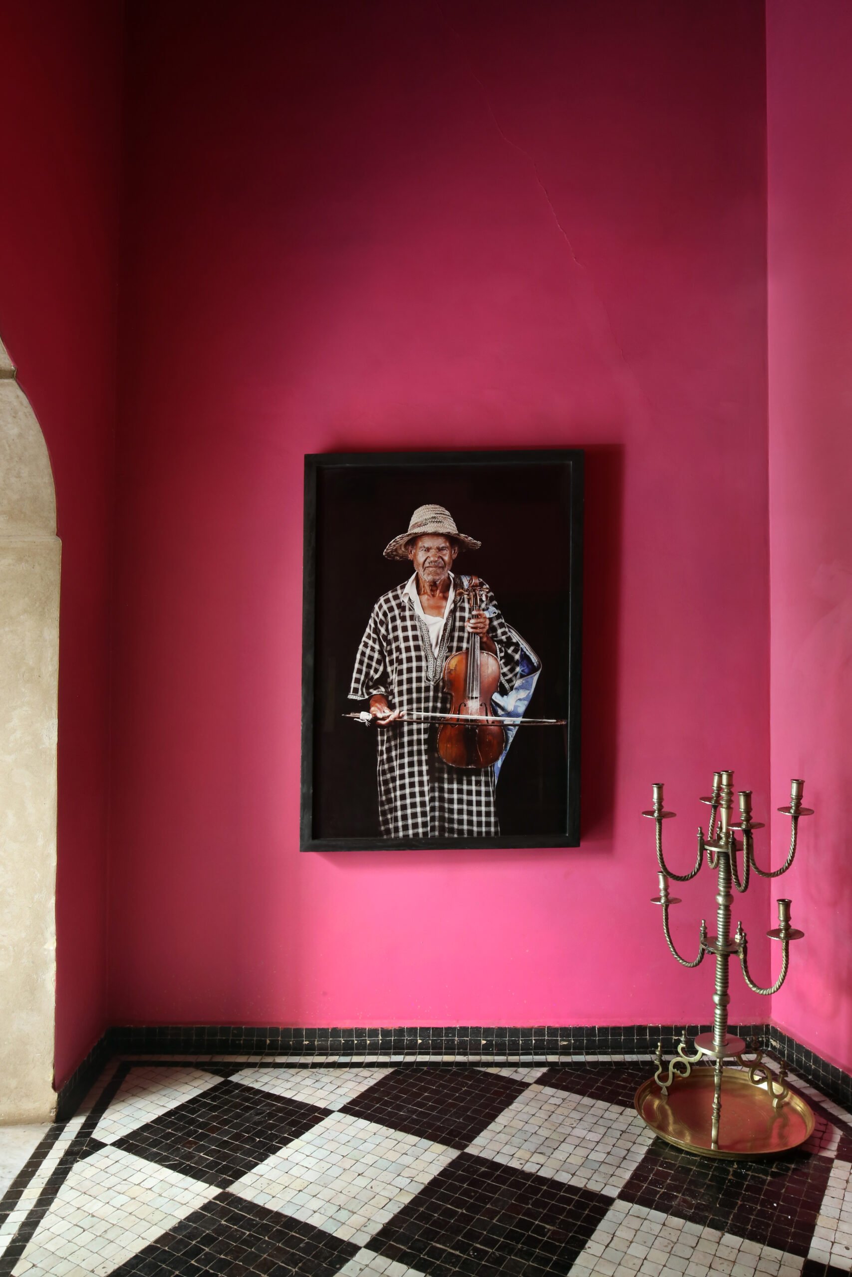 A framed portrait on a hot-pink wall above a brass candelabra