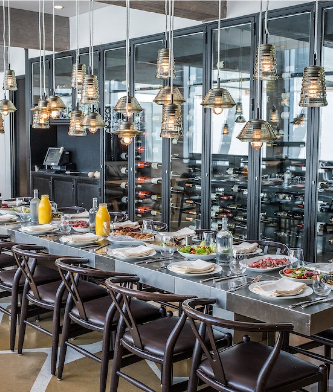The chef's restaurant, a long table under woven pendant lights with a wine wall behind