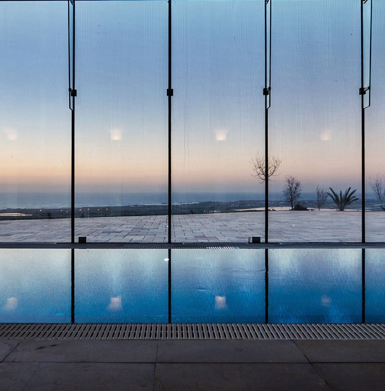 The indoor pool at dusk, glazed to the coastal plain and the sea