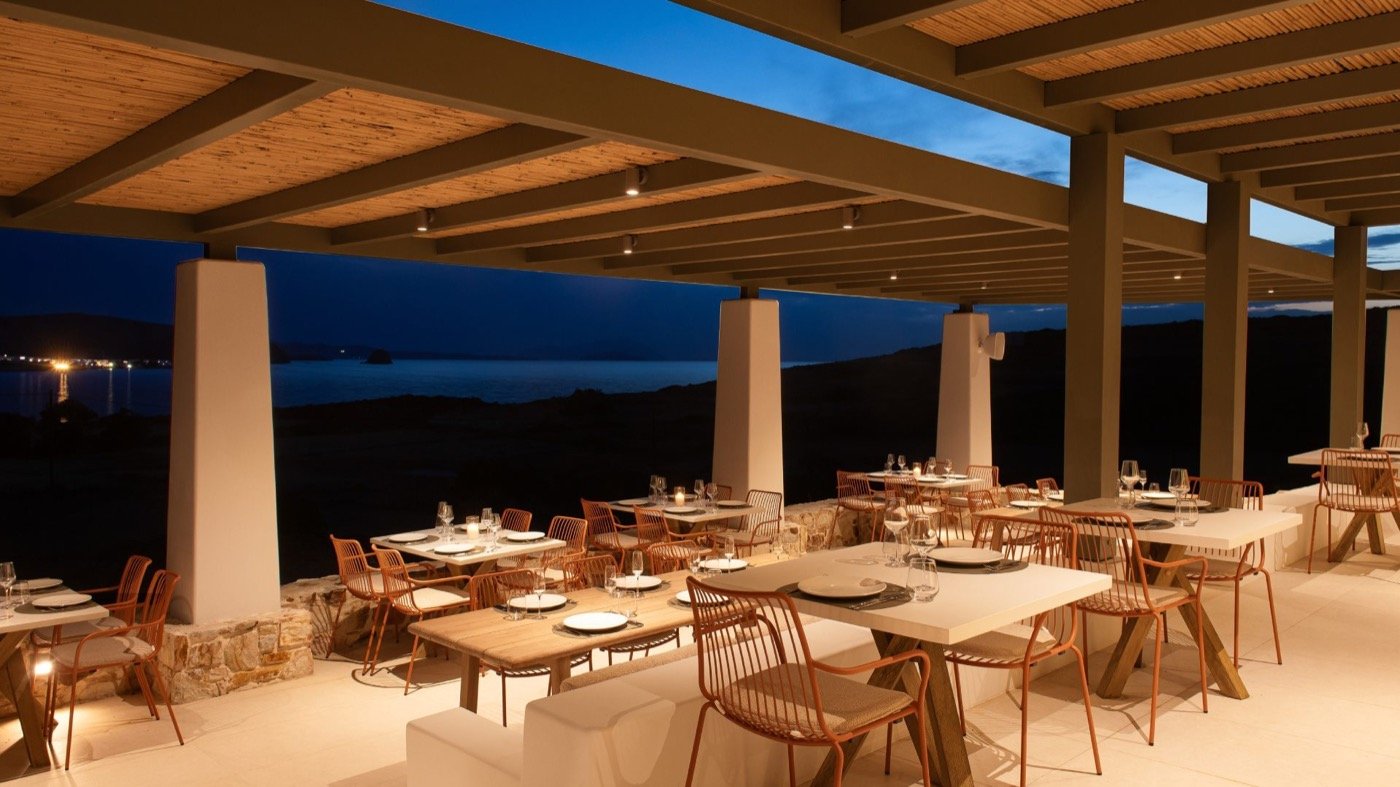 amoni, the hotel restaurant laid for dinner under the pergola at dusk, Milos across the water