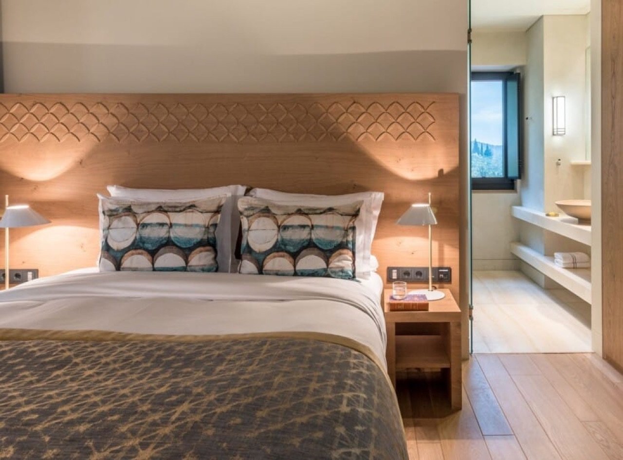 A room with a carved oak headboard opening to the Taygetos slope