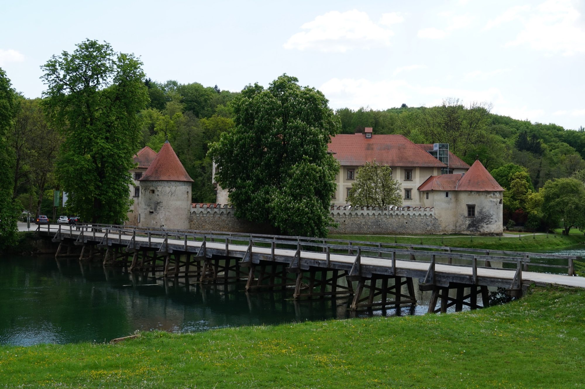 Grad Otočec seen from across the Krka in spring, the long wooden bridge crossing to the island castle