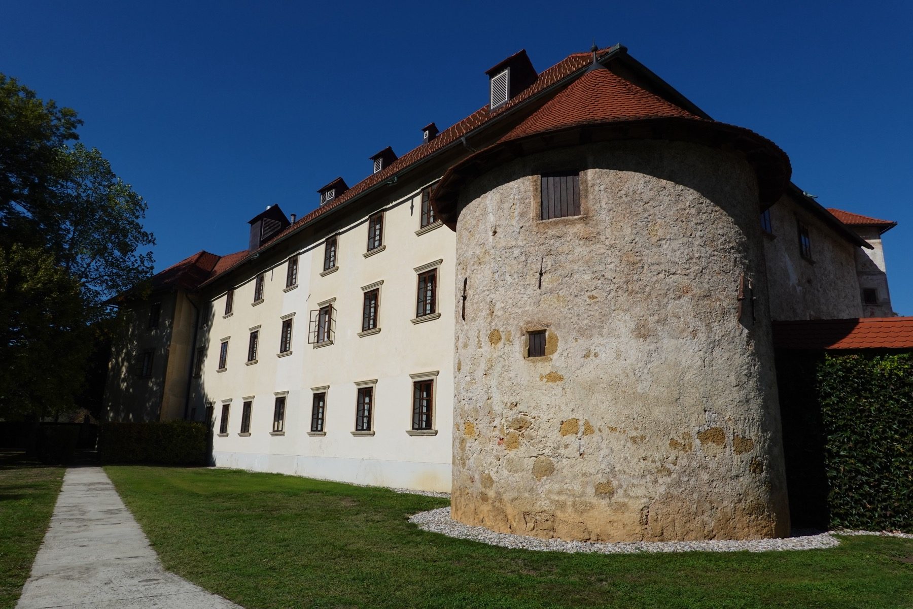 A round stone defensive tower at Grad Otočec, its old masonry against the castle wing