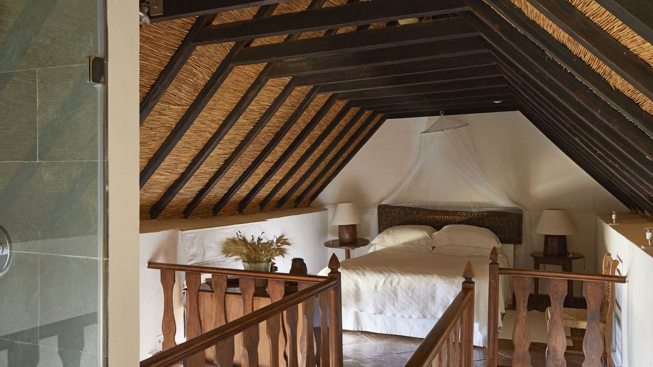 A bedroom under a reed and beam ceiling with a canopy of muslin over the bed