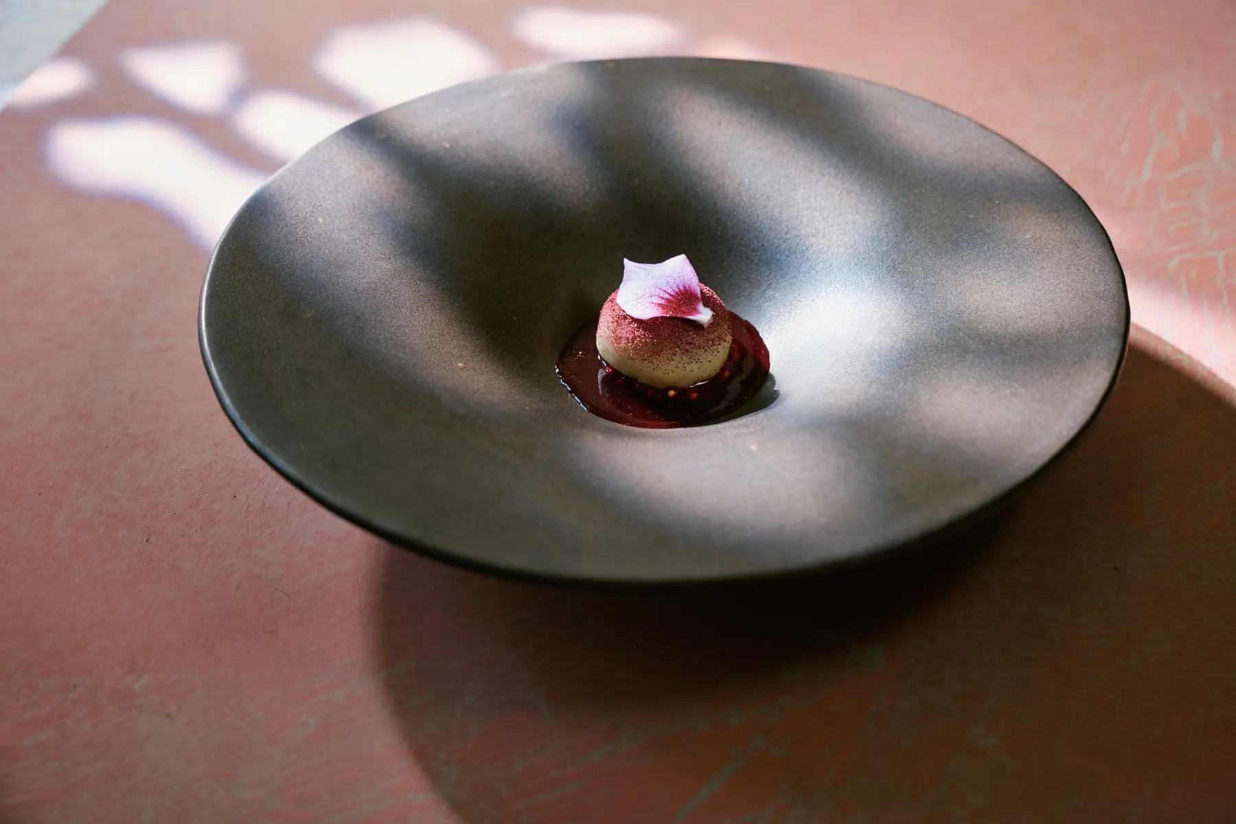 A dessert plated in a dark bowl with a single flower