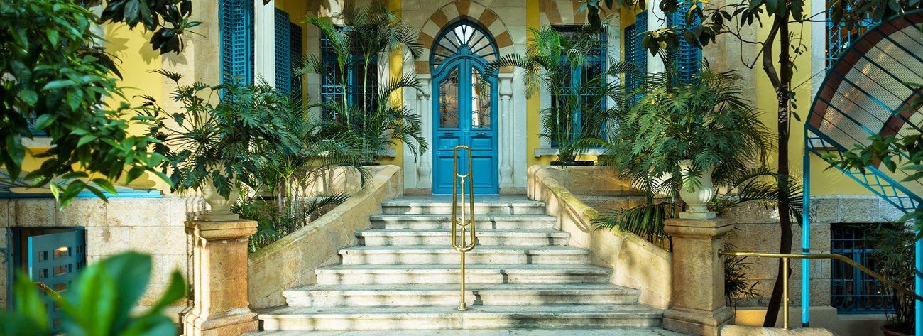 The blue front door of the 1930s mansion, up a flight of stone steps between palms