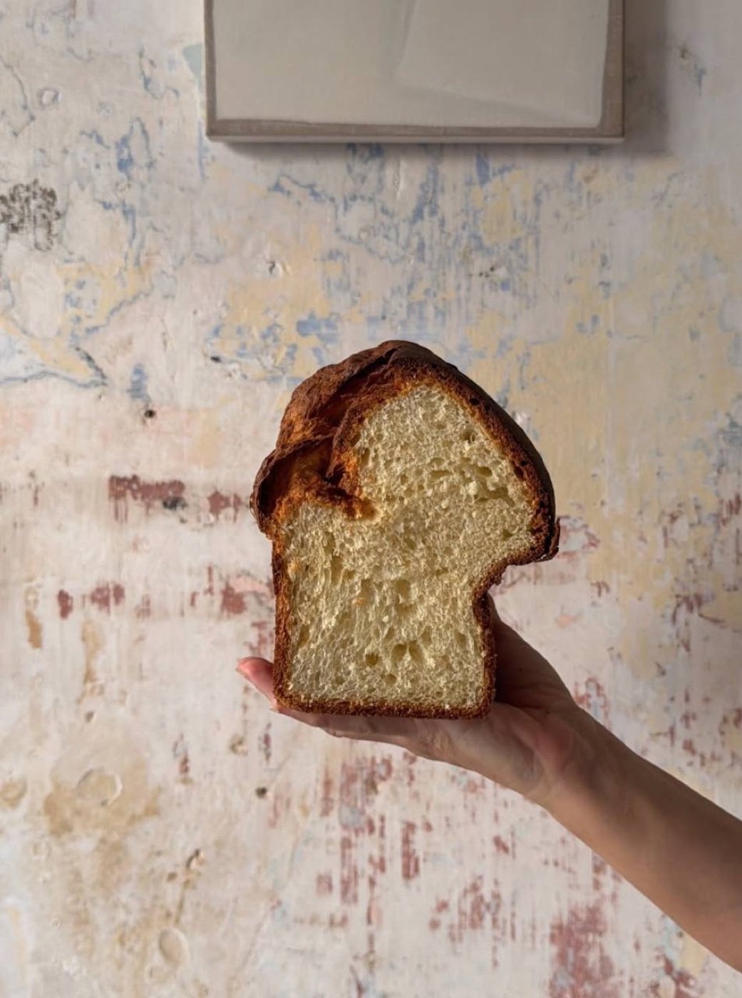 A thick slice of golden brioche from Burro, held against a plaster wall